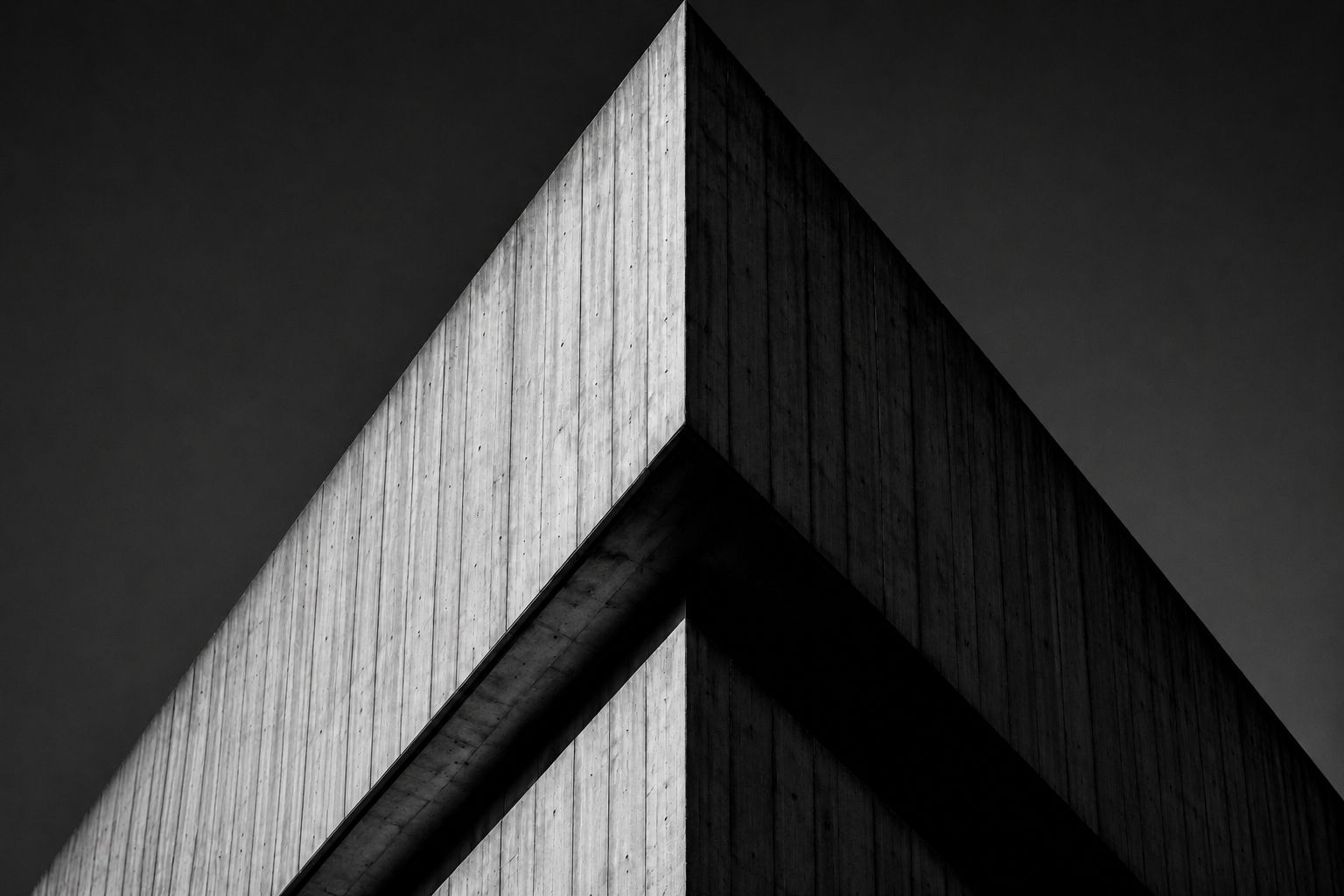 Low-angle shot of a monolithic concrete structure with sharp geometric edges against a stark sky. The brutalist architecture features raw textures and heavy shadows, projecting institutional power and permanence.